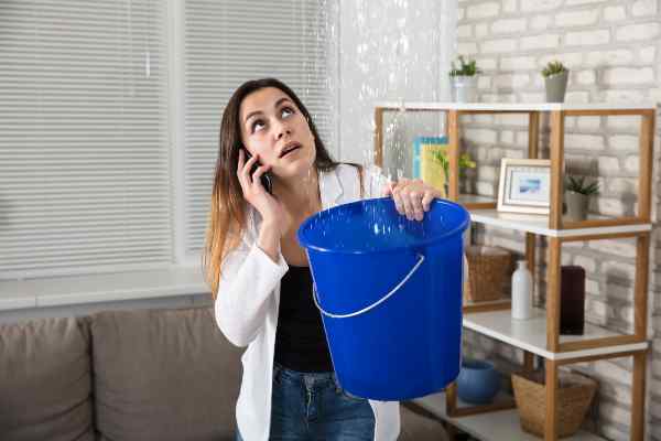 woman holding bucket in air to catch water leaking fro ceiling